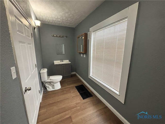 bathroom with baseboards, visible vents, toilet, wood finished floors, and a textured ceiling