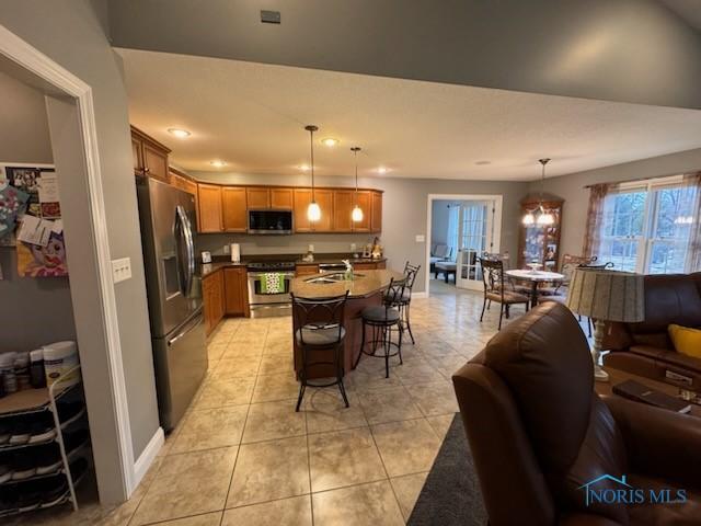 kitchen featuring open floor plan, a breakfast bar, light tile patterned floors, brown cabinetry, and stainless steel appliances