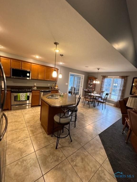 kitchen with light tile patterned floors, brown cabinetry, a sink, stainless steel appliances, and dark countertops