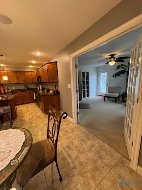 dining area with ceiling fan, baseboards, light colored carpet, and light tile patterned flooring