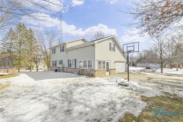 snow covered house with a trampoline, concrete driveway, and a garage