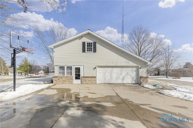 view of property exterior featuring a garage, a trampoline, concrete driveway, and brick siding