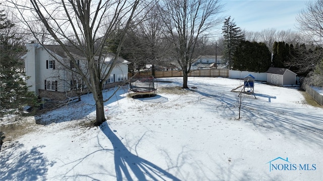 yard covered in snow with an outbuilding, a fenced backyard, a fire pit, and a storage unit