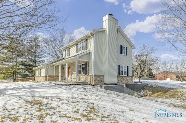 view of snowy exterior featuring covered porch, brick siding, and a chimney