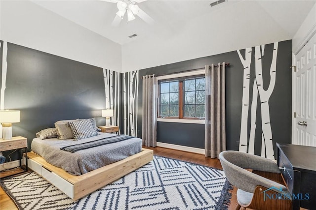 bedroom with a ceiling fan, visible vents, baseboards, and wood finished floors