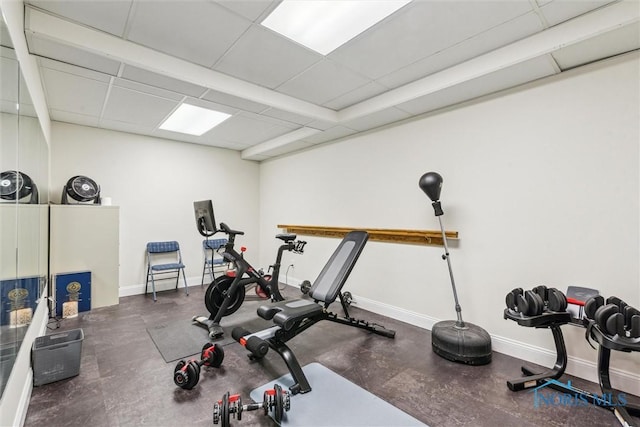 workout room with a paneled ceiling and baseboards