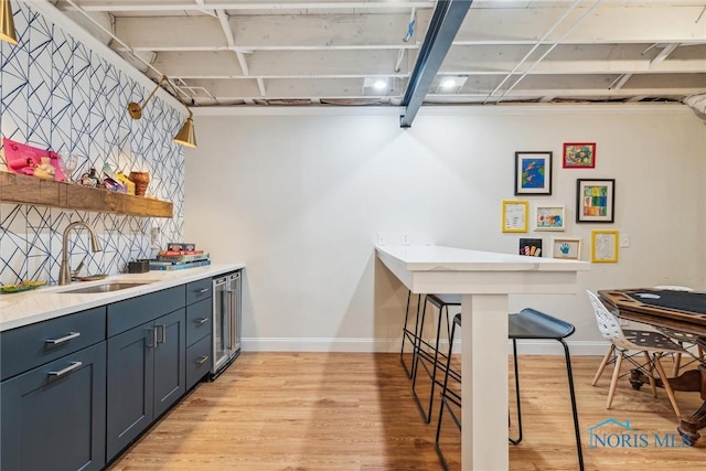 kitchen featuring open shelves, light wood-style flooring, a sink, beverage cooler, and baseboards