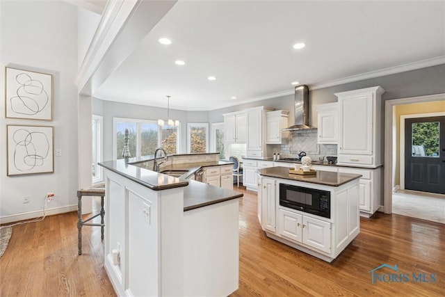 kitchen with black microwave, a sink, a large island, wall chimney exhaust hood, and dark countertops