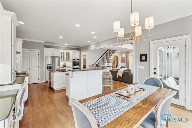 dining room featuring recessed lighting, an inviting chandelier, ornamental molding, light wood-type flooring, and stairs