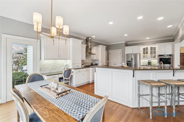 kitchen featuring stainless steel appliances, dark countertops, white cabinetry, and wall chimney exhaust hood