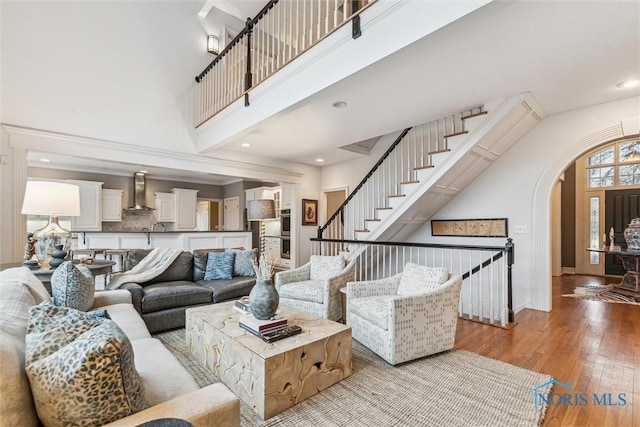 living room featuring arched walkways, a towering ceiling, hardwood / wood-style flooring, stairway, and recessed lighting