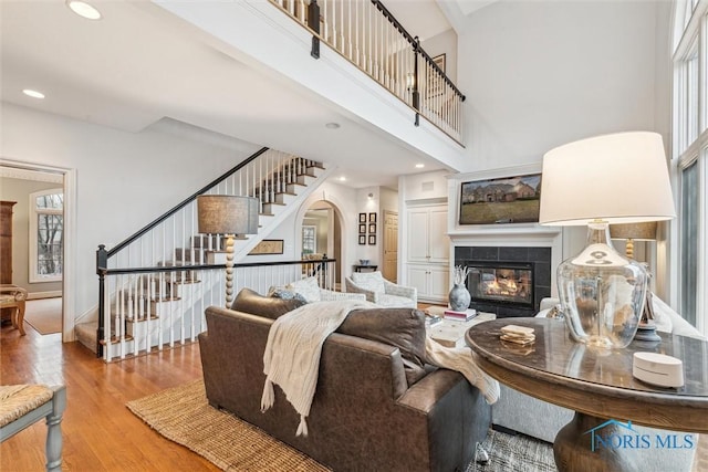 living area featuring a towering ceiling, wood finished floors, stairs, a fireplace, and recessed lighting