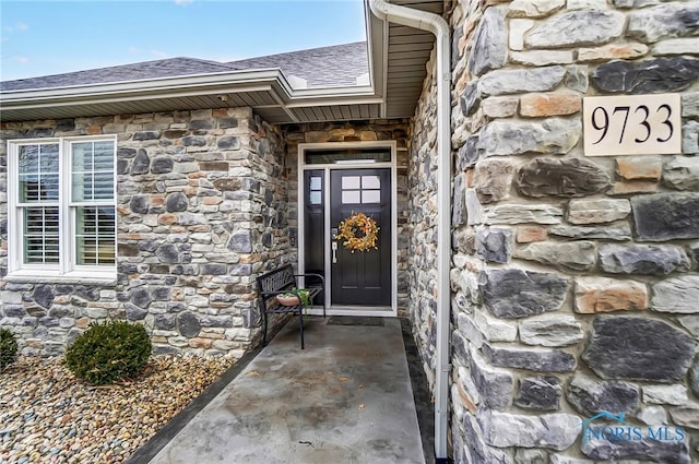 doorway to property with stone siding and a shingled roof