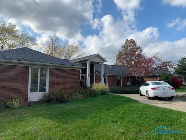 single story home featuring a shingled roof, brick siding, driveway, and a front lawn