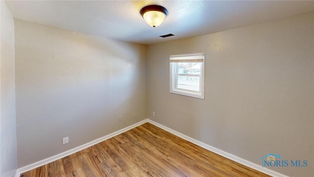 empty room featuring baseboards, visible vents, and wood finished floors