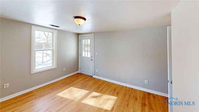 empty room featuring a textured ceiling, light wood-type flooring, visible vents, and baseboards