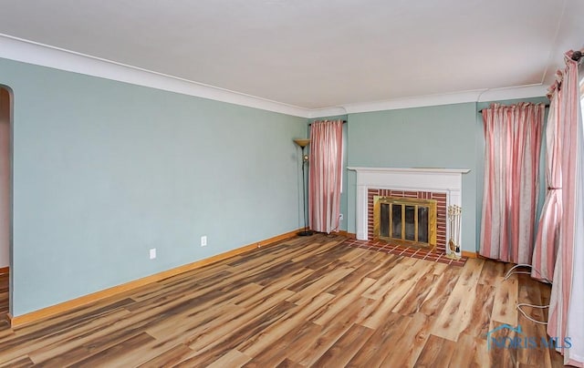 unfurnished living room featuring baseboards, arched walkways, ornamental molding, wood finished floors, and a fireplace