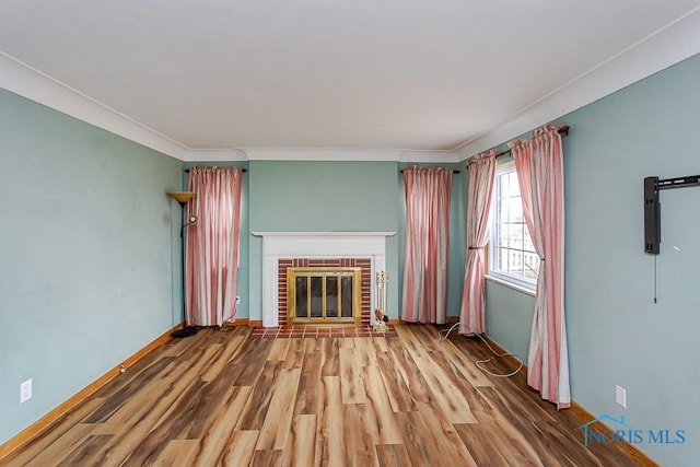 unfurnished living room featuring a brick fireplace, crown molding, baseboards, and wood finished floors