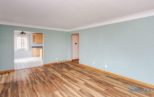 unfurnished living room with crown molding, wood finished floors, visible vents, and baseboards