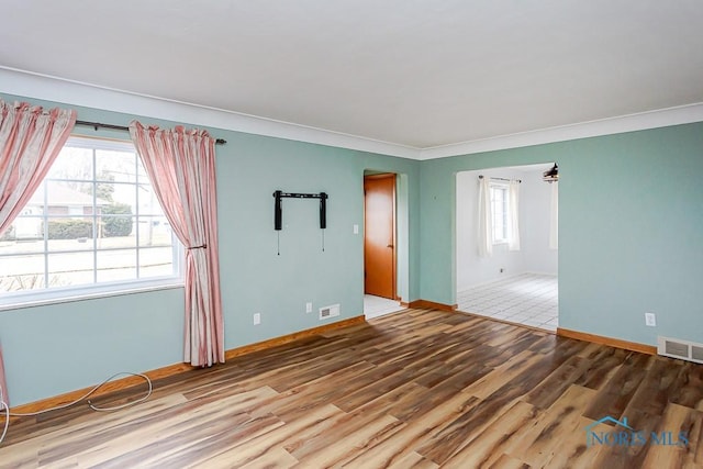 unfurnished room with visible vents, crown molding, baseboards, and wood finished floors