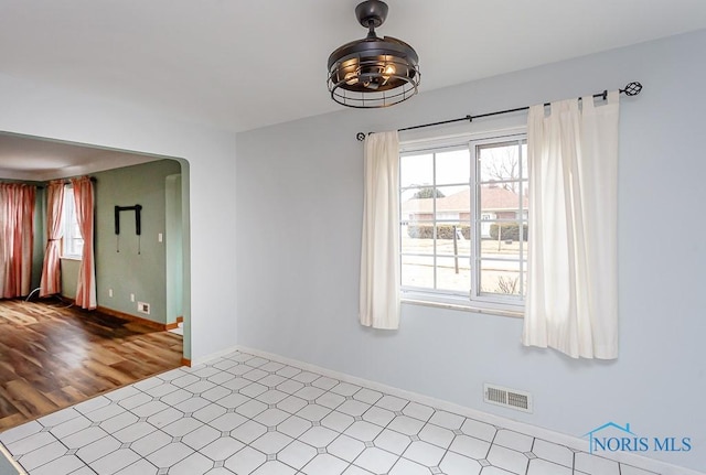 spare room featuring arched walkways, visible vents, baseboards, and tile patterned floors