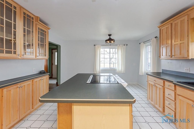 kitchen featuring dark countertops, glass insert cabinets, a center island, black electric stovetop, and light floors