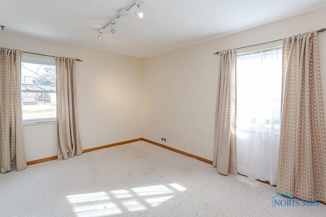 carpeted spare room featuring track lighting and baseboards