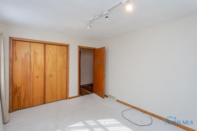 unfurnished bedroom with baseboards, visible vents, rail lighting, carpet flooring, and a closet