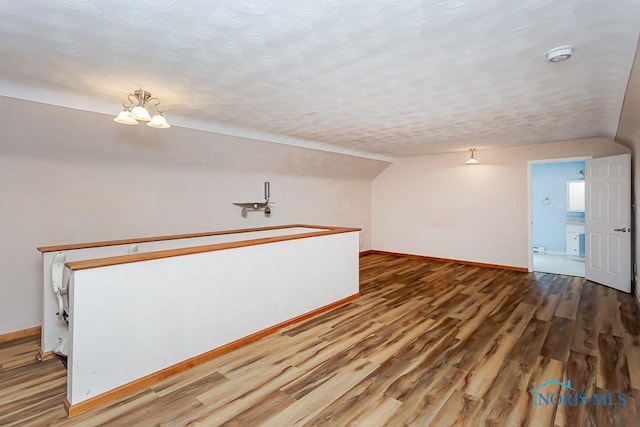 bonus room featuring vaulted ceiling, a textured ceiling, wood finished floors, and baseboards