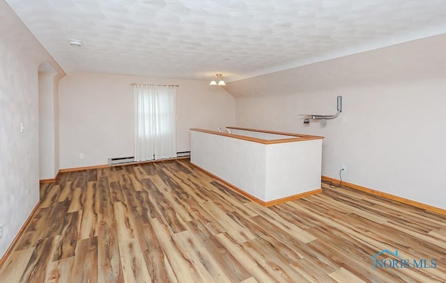 unfurnished room featuring baseboards, a baseboard radiator, wood finished floors, vaulted ceiling, and a textured ceiling