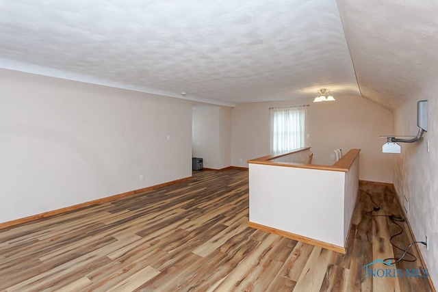 empty room featuring vaulted ceiling, a textured ceiling, wood finished floors, and baseboards