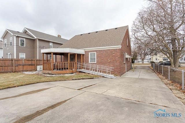 back of house with a deck, brick siding, fence, roof with shingles, and a lawn