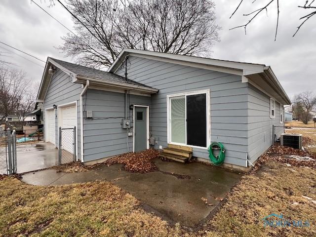 back of house with entry steps, central AC unit, an attached garage, and fence