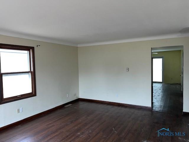 unfurnished room with plenty of natural light, baseboards, dark wood-type flooring, and ornamental molding