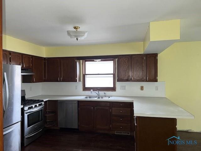 kitchen with light countertops, appliances with stainless steel finishes, a sink, a peninsula, and under cabinet range hood