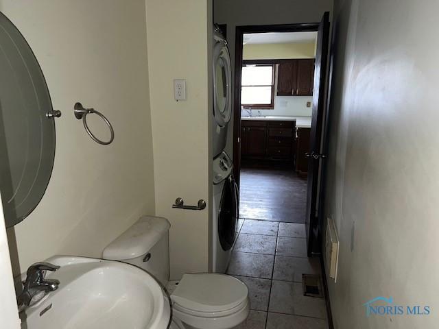 bathroom featuring toilet, stacked washer and dryer, and a sink