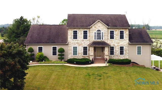 colonial inspired home featuring a front lawn and roof with shingles