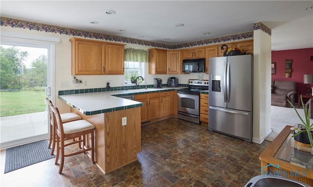 kitchen featuring a peninsula, stone finish flooring, stainless steel appliances, a kitchen bar, and a sink