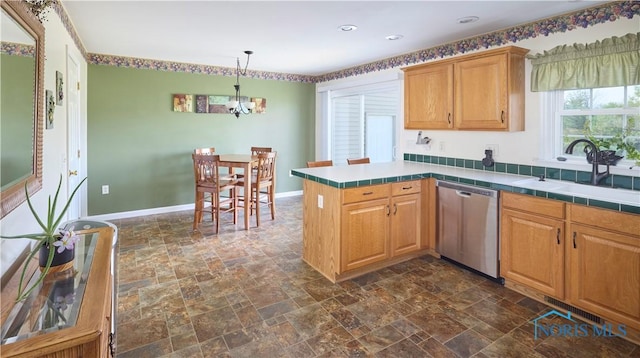 kitchen with baseboards, stone finish floor, a peninsula, stainless steel dishwasher, and a sink