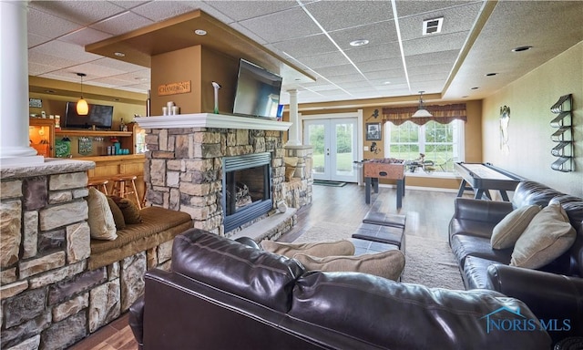 living room featuring a drop ceiling, wood finished floors, visible vents, french doors, and ornate columns