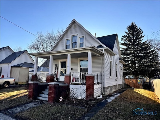 bungalow-style home with covered porch, fence, and roof with shingles