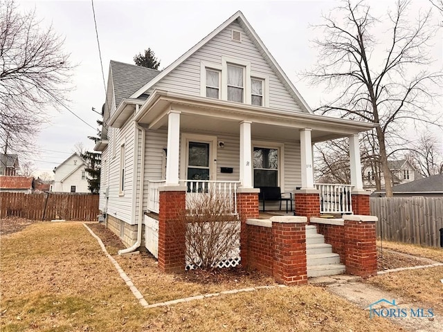 bungalow featuring covered porch, a shingled roof, and fence