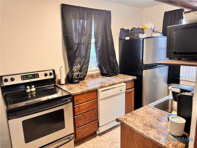 kitchen featuring light tile patterned floors, light countertops, appliances with stainless steel finishes, and brown cabinetry