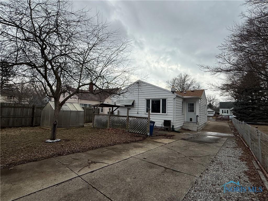 rear view of house with a greenhouse, entry steps, an outbuilding, and fence private yard