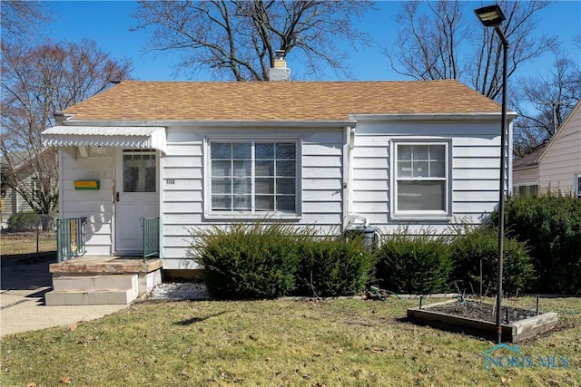 bungalow-style house featuring a shingled roof, a chimney, a front lawn, and a garden