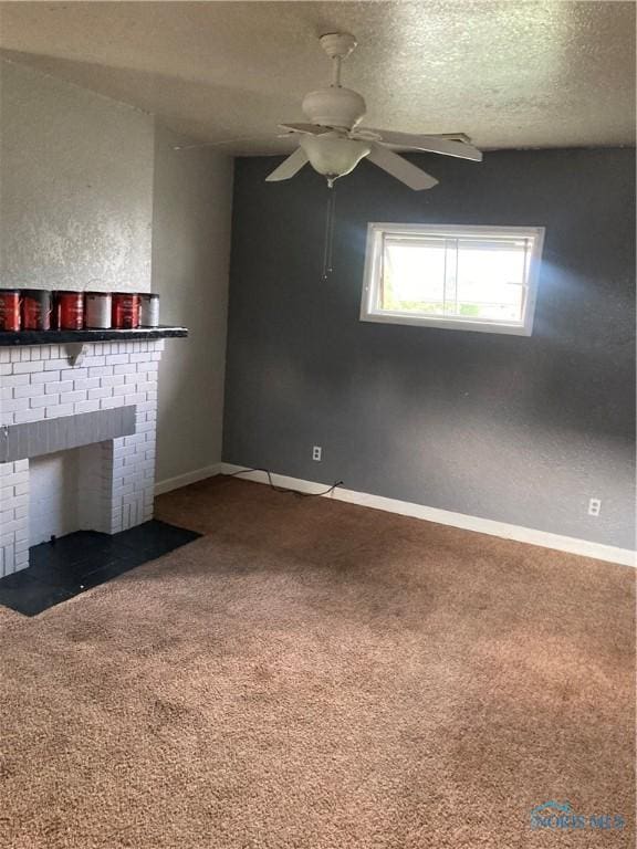 unfurnished living room featuring baseboards, ceiling fan, a textured ceiling, carpet floors, and a brick fireplace