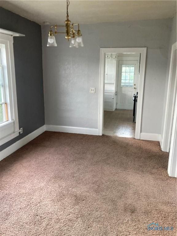 unfurnished room featuring a notable chandelier, baseboards, and carpet flooring