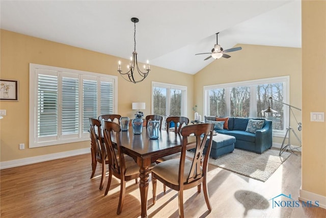 dining area with lofted ceiling, ceiling fan with notable chandelier, wood finished floors, and baseboards