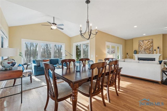 dining area featuring a notable chandelier, recessed lighting, a fireplace, vaulted ceiling, and light wood-type flooring