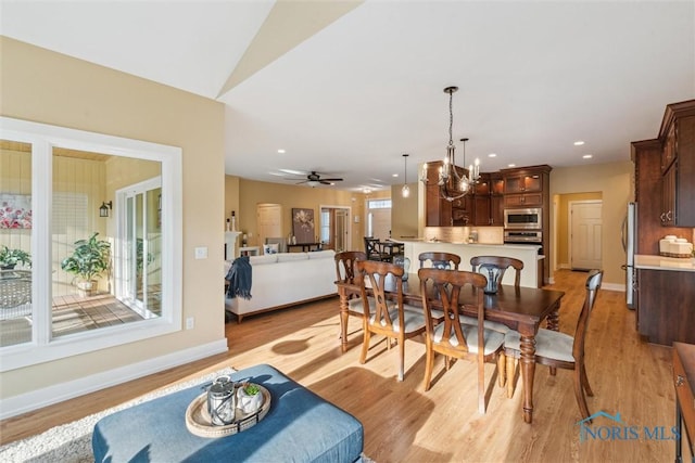 dining area with baseboards, light wood finished floors, and ceiling fan with notable chandelier